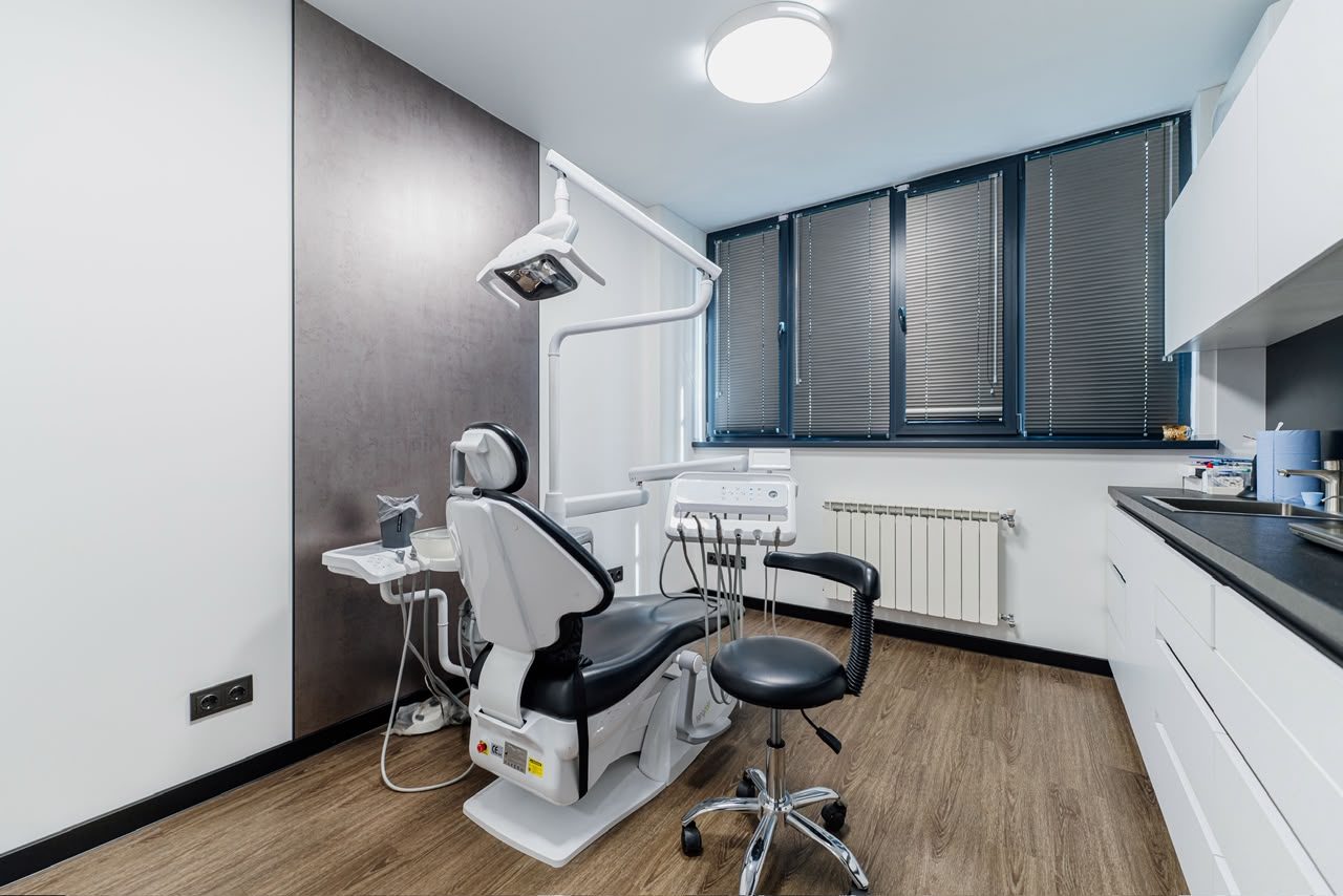 Treatment room at ESTHEMAX: the dental chair by a window with blinds, and white cabinets