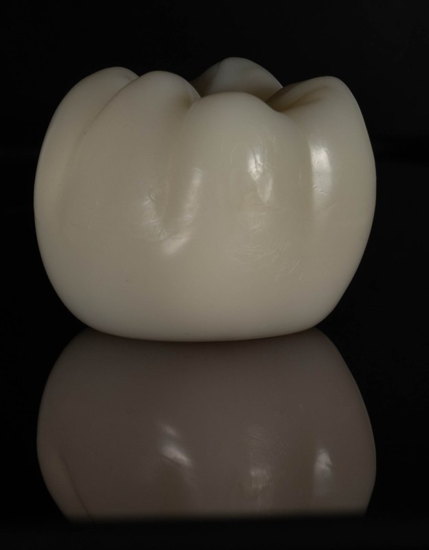 A dental crown on a black background, with its reflection